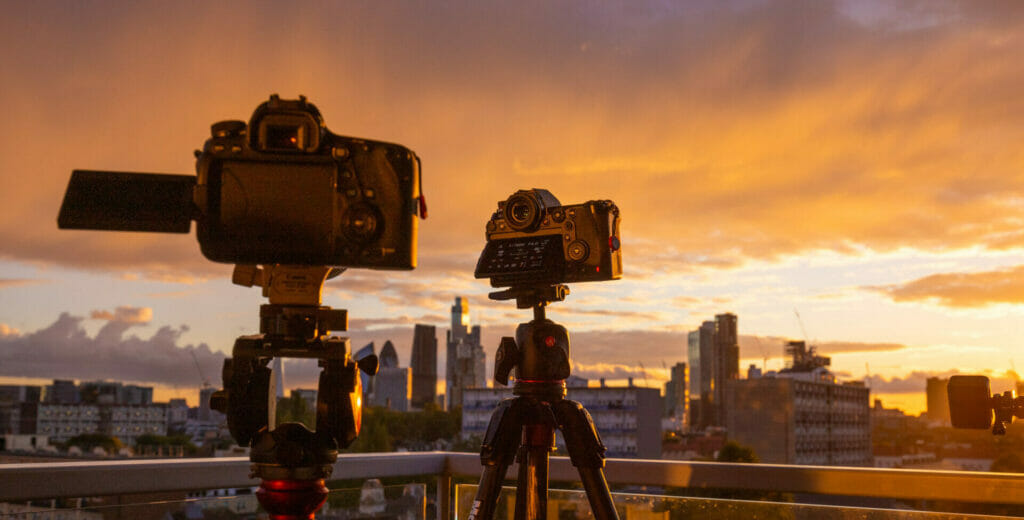 A silhouetted image of two cameras at sunset with the skyline of the city of london in the back